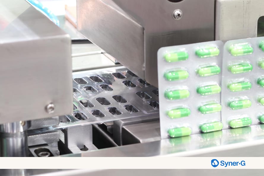 Close-up of an automated pharmaceutical packaging machine sealing green capsules into blister packs.