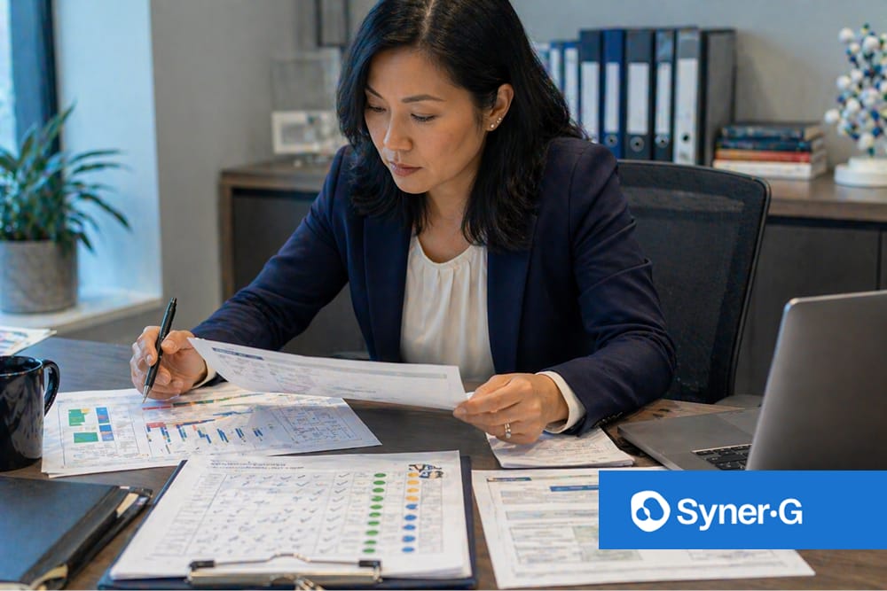 Biopharma professional reviewing printed project documents at her desk with a laptop and office files nearby